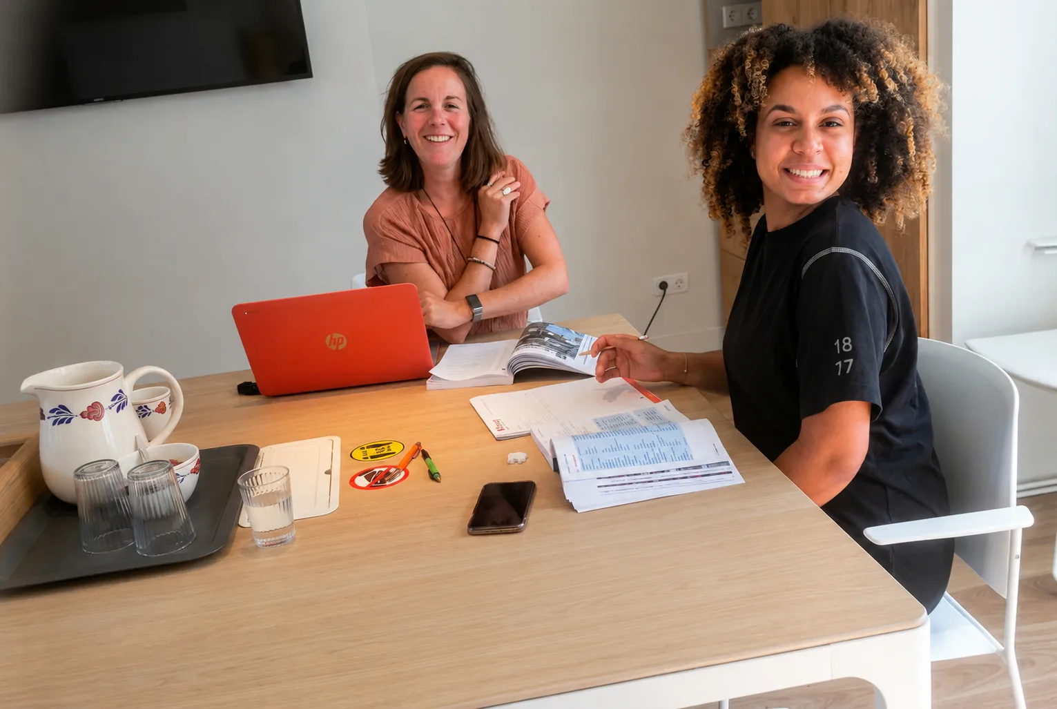 Dutch teacher and student smiling during a Dutch language lesson at the Baay classroom table in Rotterdam
